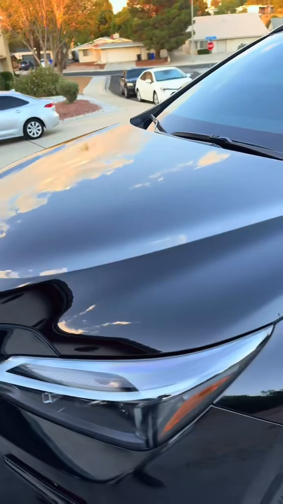 Close-up of a sleek black car headlight with suburban street background