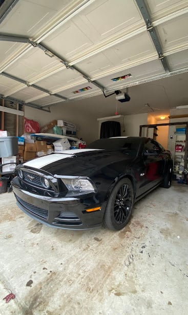 Black Ford Mustang parked inside a cluttered garage