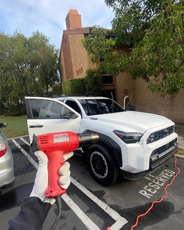 Hand holding red heat gun next to white SUV in parking lot