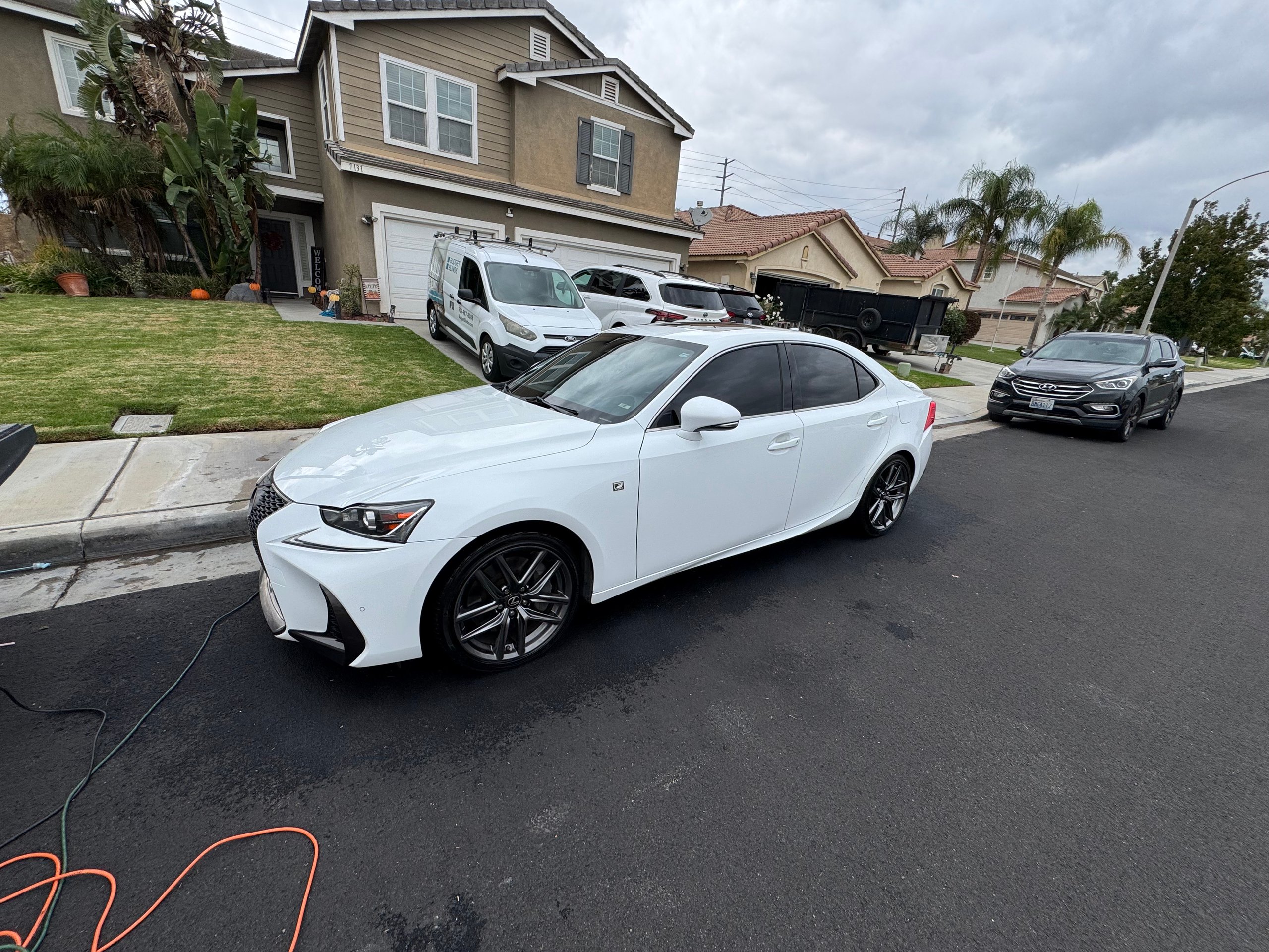 White Lexus sedan parked on suburban street with charging cable