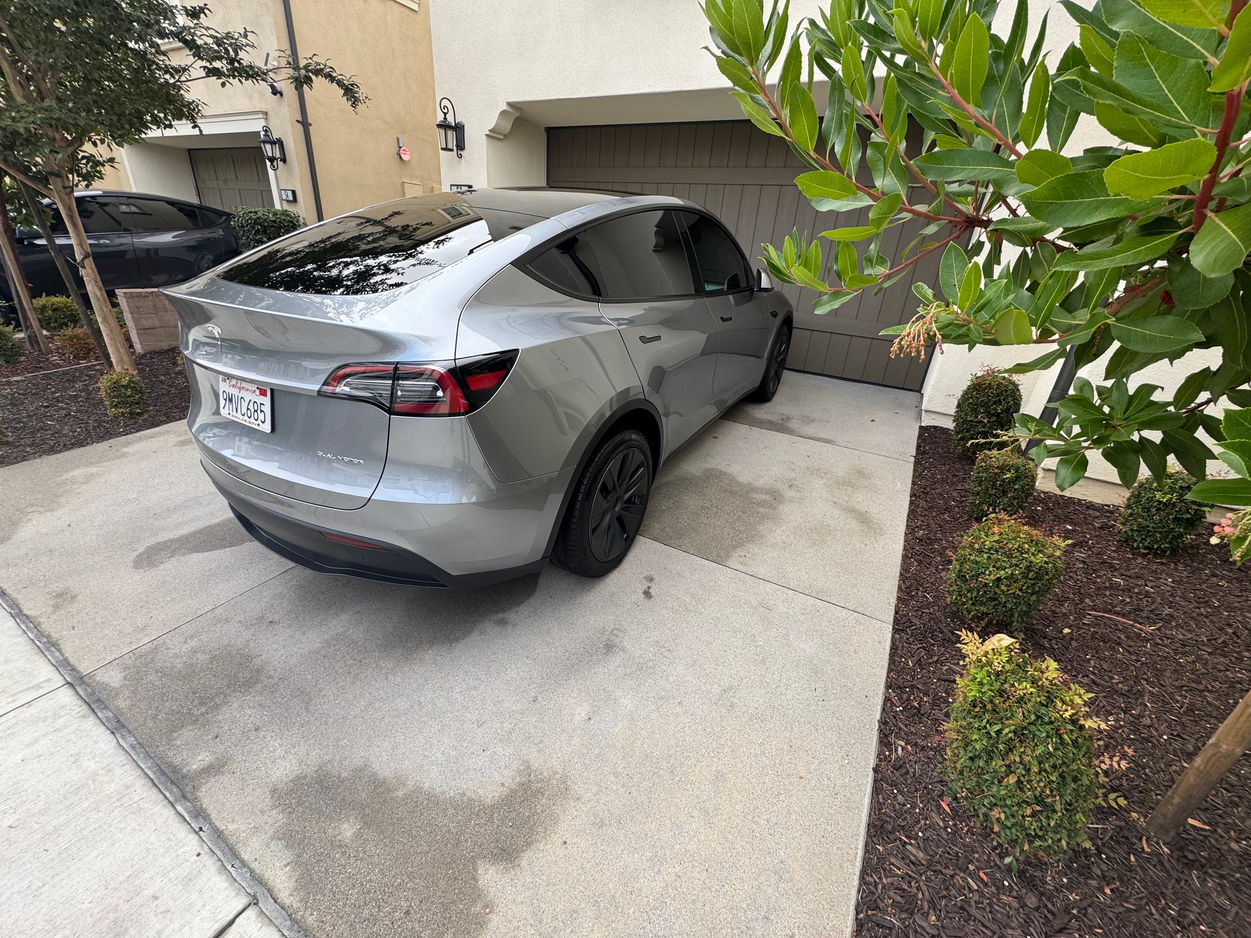Silver Tesla Model Y parked in residential driveway with landscaping