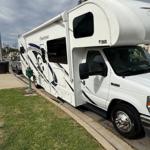 White and blue RV parked on grass near street on cloudy day